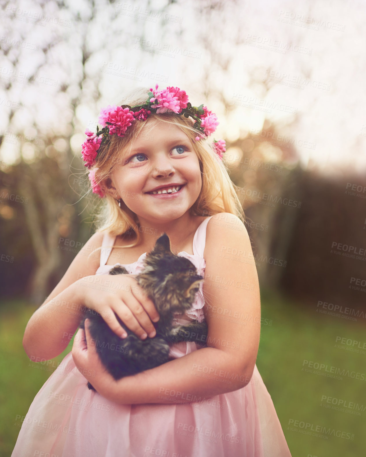 Buy stock photo Shot of a happy little girl holding a kitten and looking into the distance while standing outside in nature