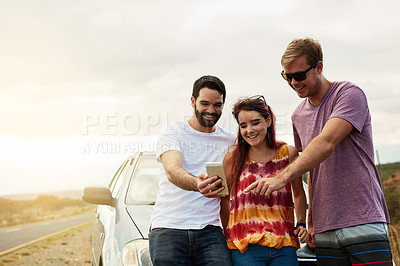 Buy stock photo Shot of a group young friends looking at photos on a cellphone while standing outside next to a road