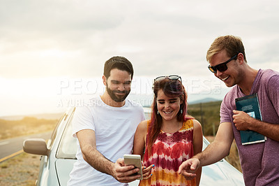 Buy stock photo Shot of a group young friends looking at photos on a cellphone while standing outside next to a road
