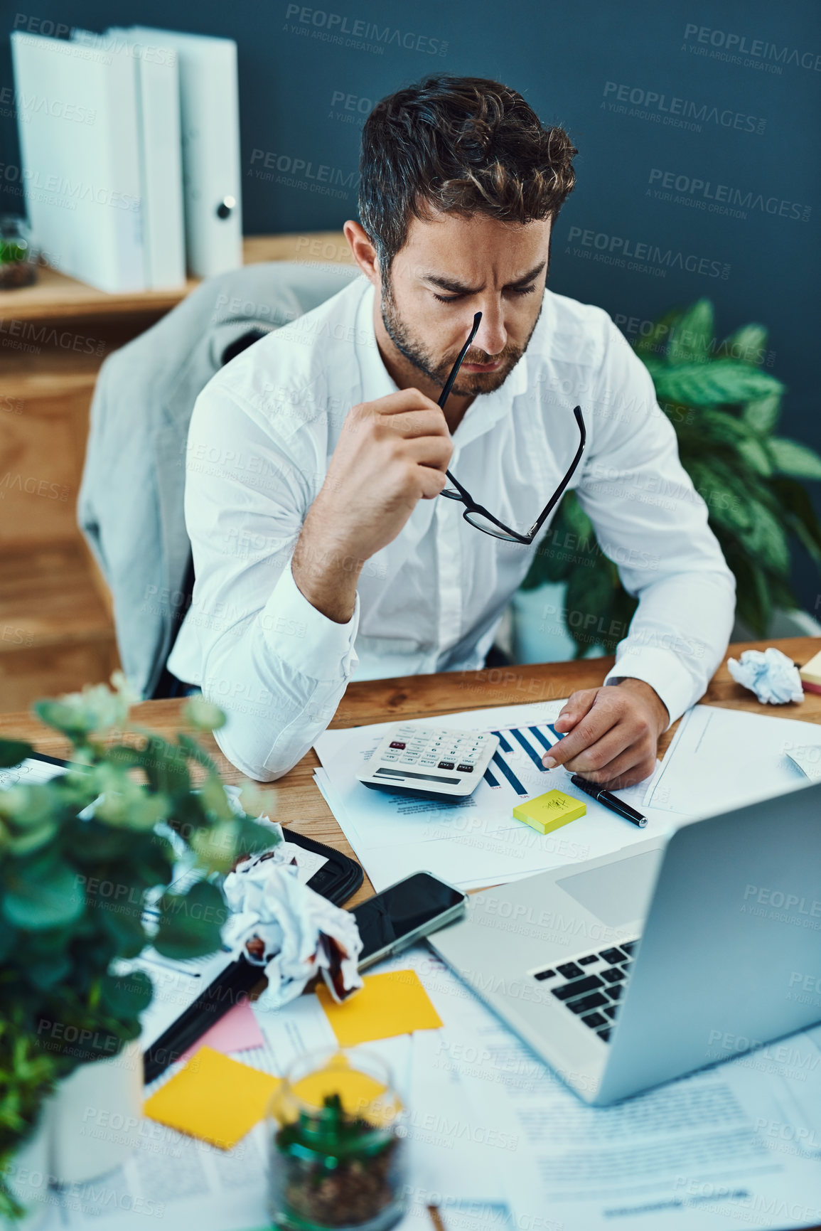 Buy stock photo Shot of a young businessman looking stressed out while working on a laptop in an office