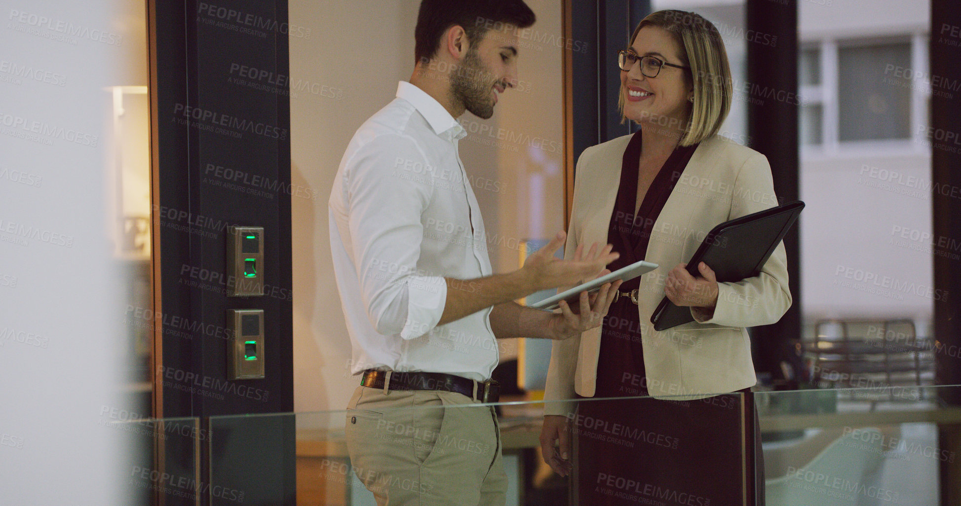 Buy stock photo Cropped shot of two businesspeople looking over a tablet while standing in the office lobby
