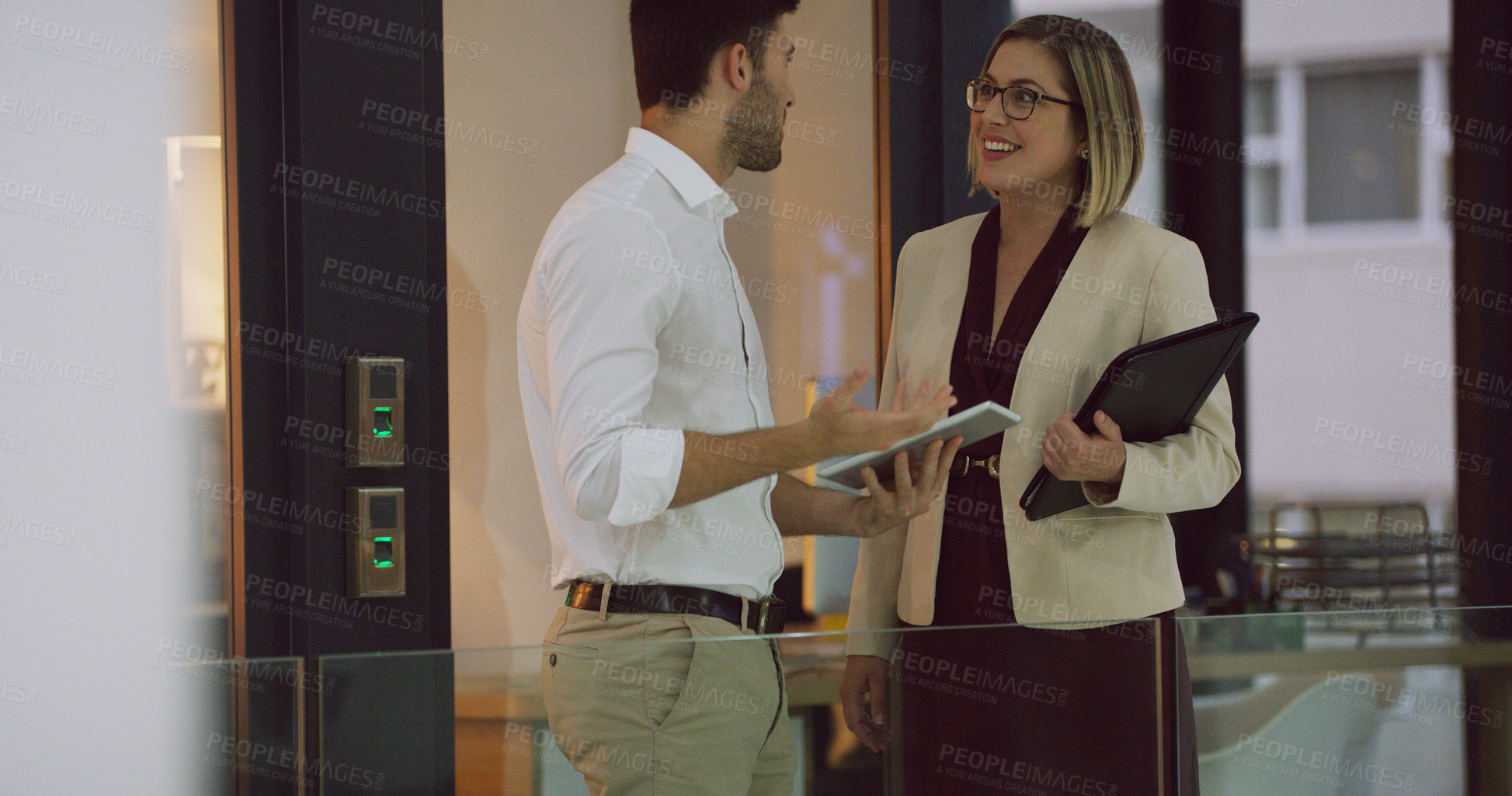 Buy stock photo Cropped shot of two businesspeople looking over a tablet while standing in the office lobby