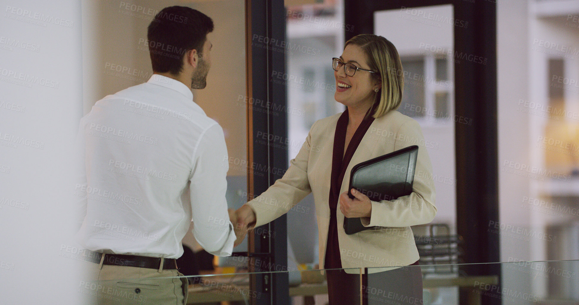 Buy stock photo Cropped shot of two businesspeople shaking hands while standing in the office lobby