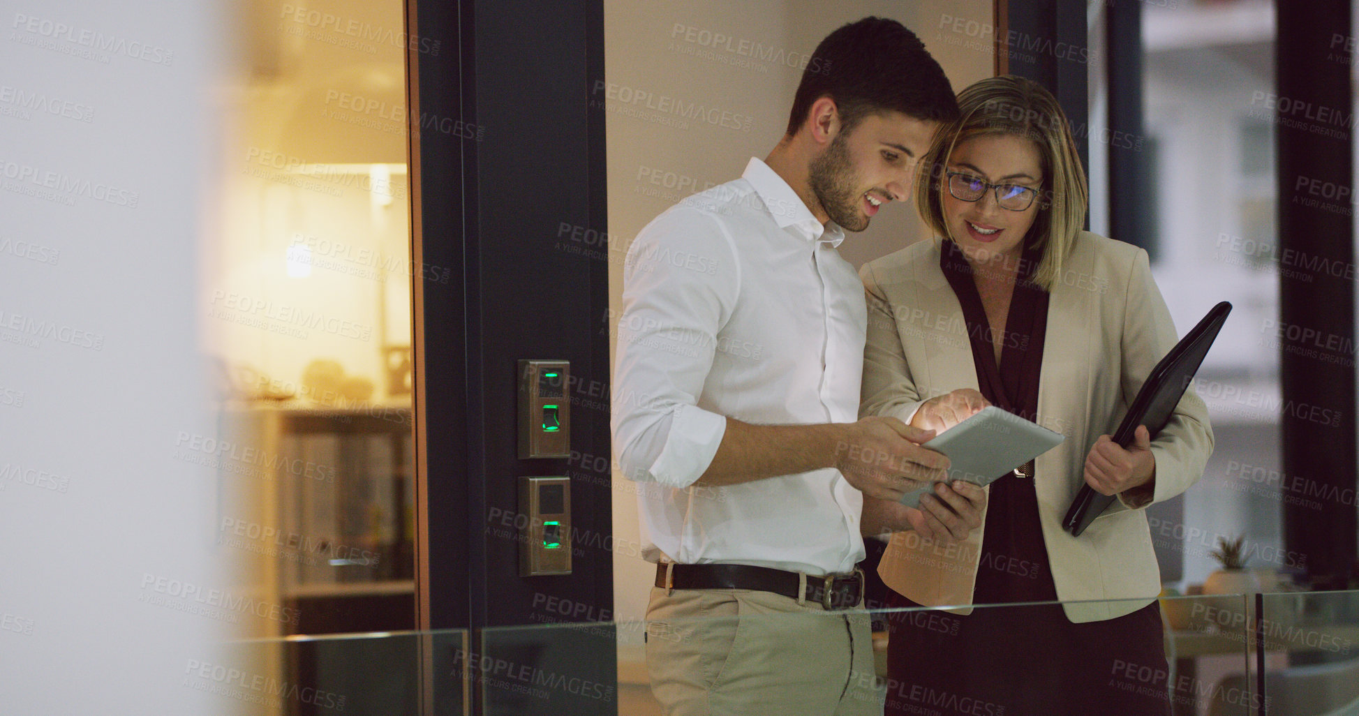 Buy stock photo Cropped shot of two businesspeople looking over a tablet while standing in the office lobby