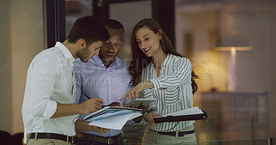 Buy stock photo Cropped shot of three businesspeople looking over a tablet while standing in the office lobby