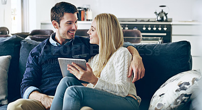 Buy stock photo Cropped shot of an affectionate young couple using a digital tablet while sitting on their sofa at home