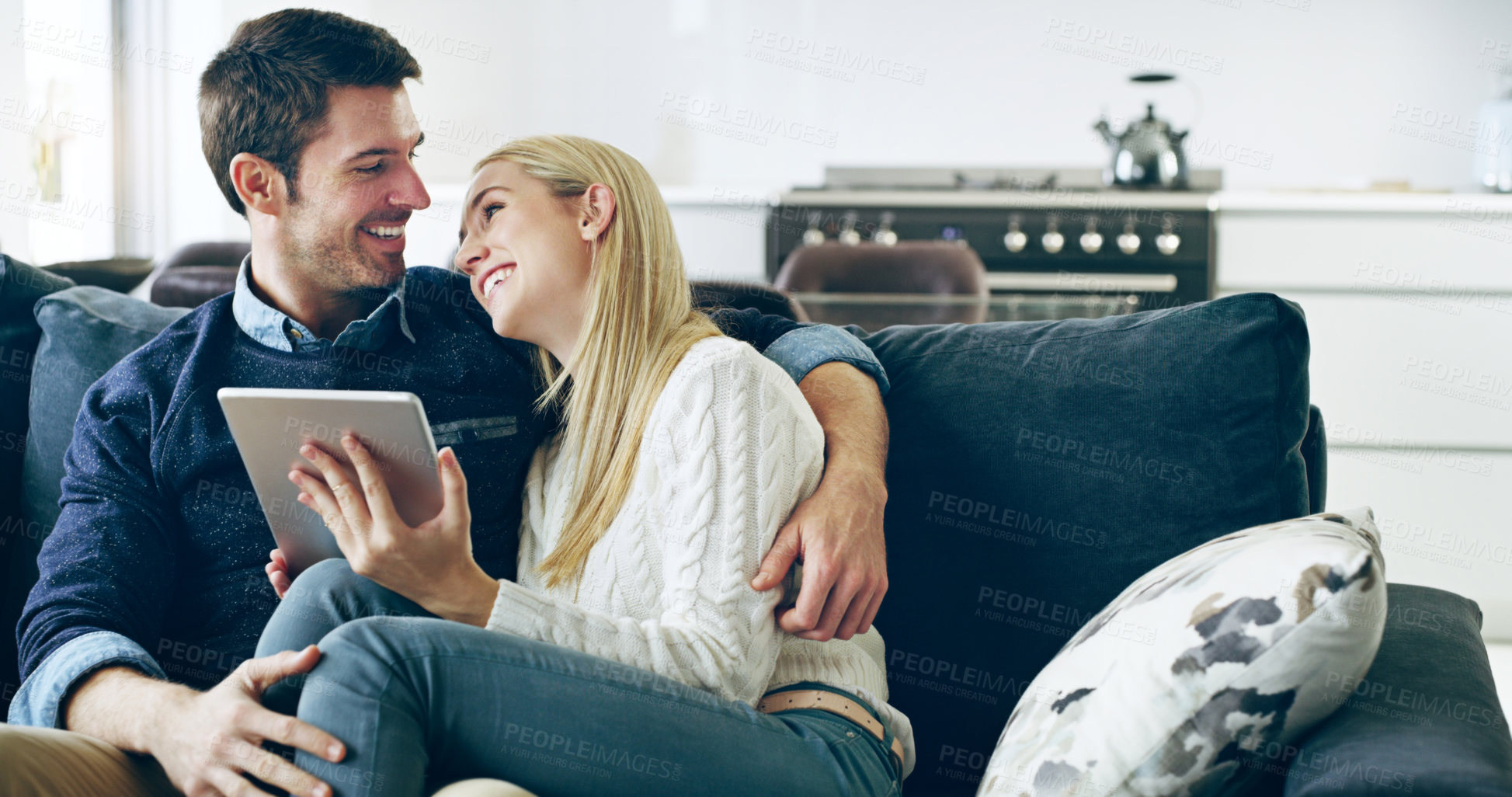 Buy stock photo Cropped shot of an affectionate young couple using a digital tablet while sitting on their sofa at home