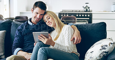 Buy stock photo Cropped shot of an affectionate young couple using a digital tablet while sitting on their sofa at home