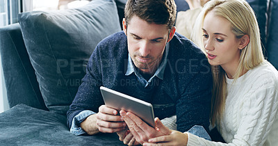 Buy stock photo Cropped shot of an affectionate young couple using a digital tablet while lying on their sofa at home