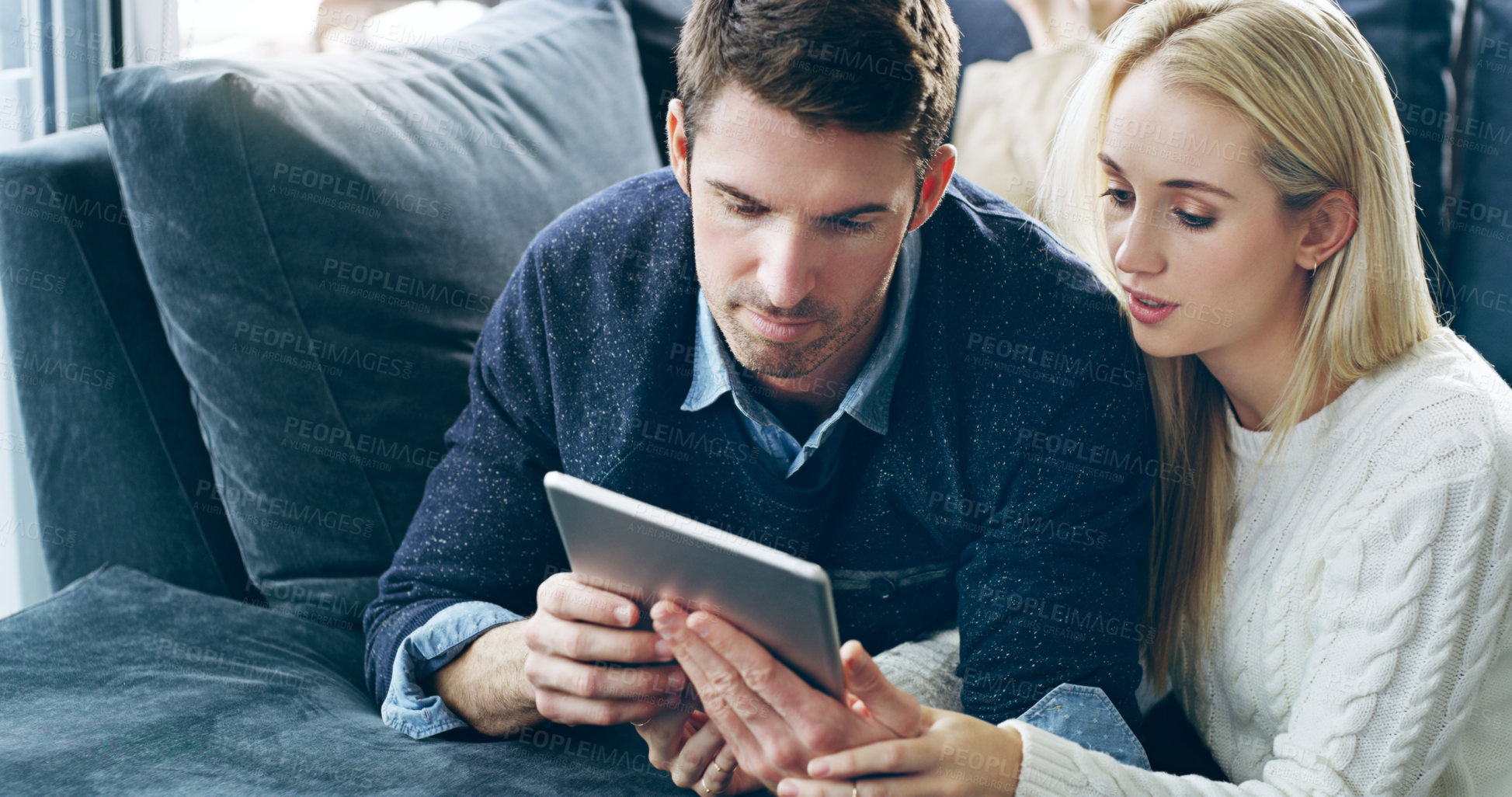 Buy stock photo Cropped shot of an affectionate young couple using a digital tablet while lying on their sofa at home