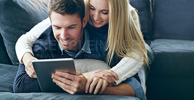 Buy stock photo Cropped shot of an affectionate young couple using a digital tablet while lying on their sofa at home