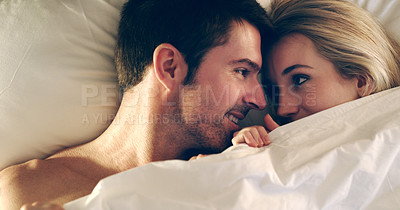 Buy stock photo High angle shot of an affectionate young couple lying in bed together