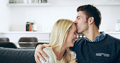 Buy stock photo Cropped shot of a handsome young man kissing his girlfriend on the forehead while sitting on their sofa at home