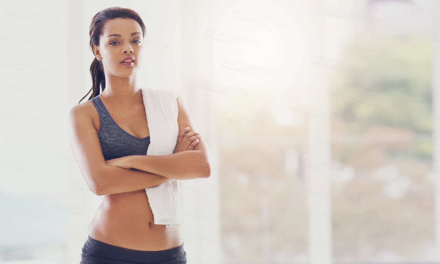 Buy stock photo Cropped portrait of an attractive young woman standing with her arms folded during a workout at home