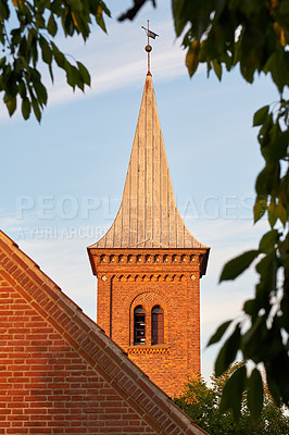 Buy stock photo Low angle of a church bell tower against a blue sky. Exterior view of a traditional old religious red brick building on a sunny day. Wall and roof of an historic house or home architecture design