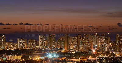 Buy stock photo High rise, skyscrapers lit up at night in a city with small houses in the foreground night beautiful modern buildings and bright glowing lights. The blue twilight skyline in the metropolis.