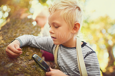 Buy stock photo Shot of an inquisitive little boy exploring the woods with a magnifying glass
