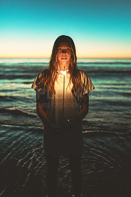 Buy stock photo Portrait of a young woman holding a sparkler at the beach at night