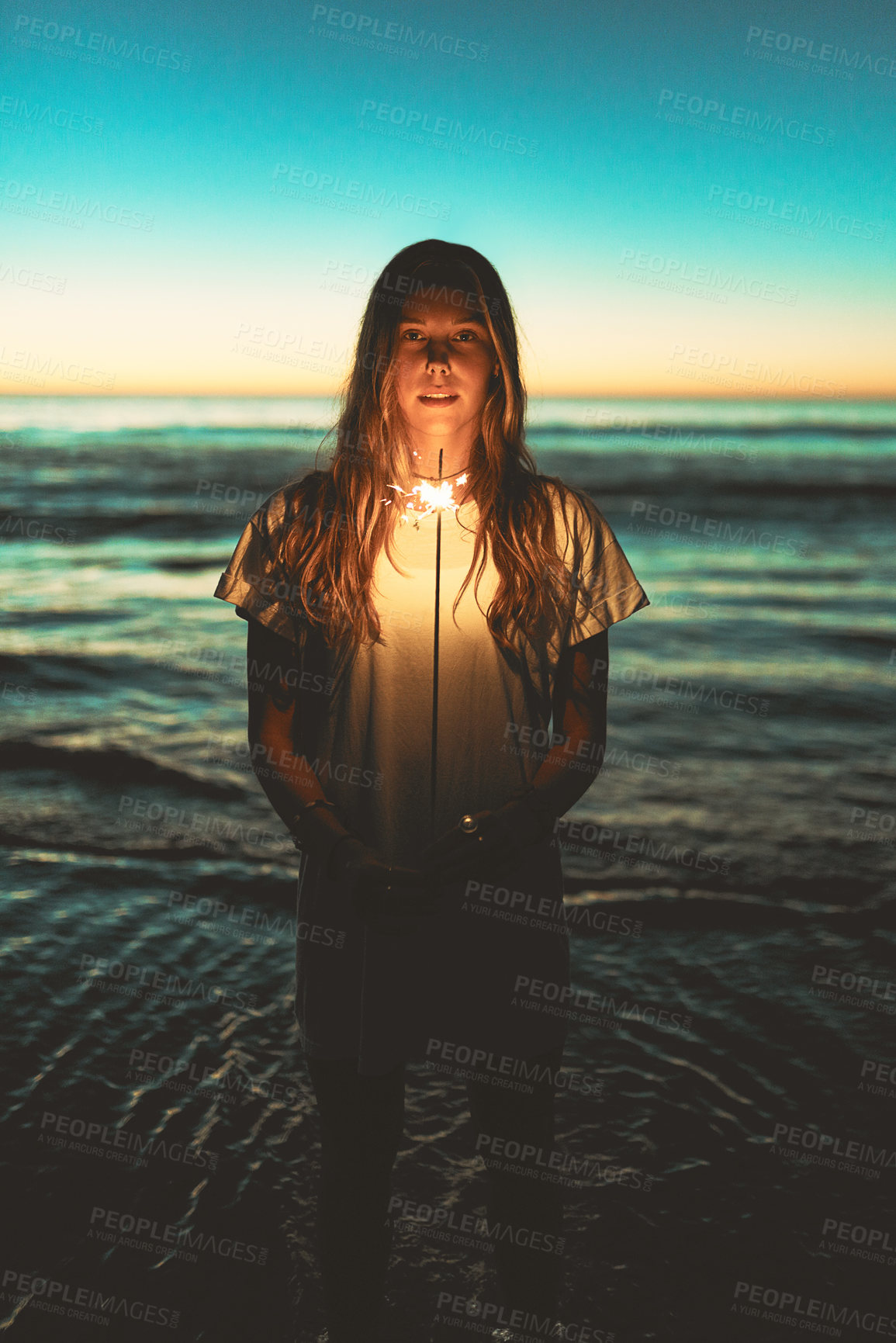 Buy stock photo Portrait of a young woman holding a sparkler at the beach at night