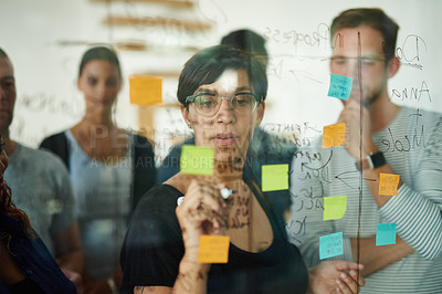 Buy stock photo Professional, smart and creative businesswoman brainstorming a strategy idea and writing on sticky notes on a transparent board with colleagues. Diverse group planning and working together in a team