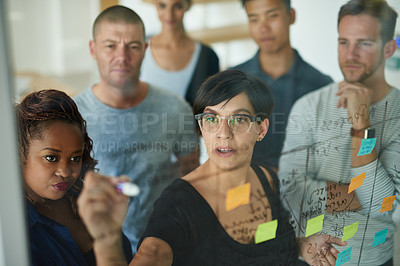 Buy stock photo Smart, thinking business people planning and writing ideas on a transparent board while working together on a group project. Busy and organized workers creating a schedule and plans with sticky notes