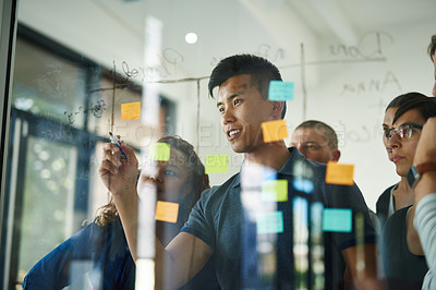 Buy stock photo Confident, smart and creative team brainstorming a strategy idea and writing on sticky notes on a transparent board in a meeting. Diverse group planning and working in close collaboration together
