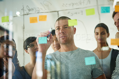 Buy stock photo Serious, smart and creative design team brainstorming a strategy idea and writing on sticky notes on a transparent board. Group planning and working in close collaboration together in a meeting