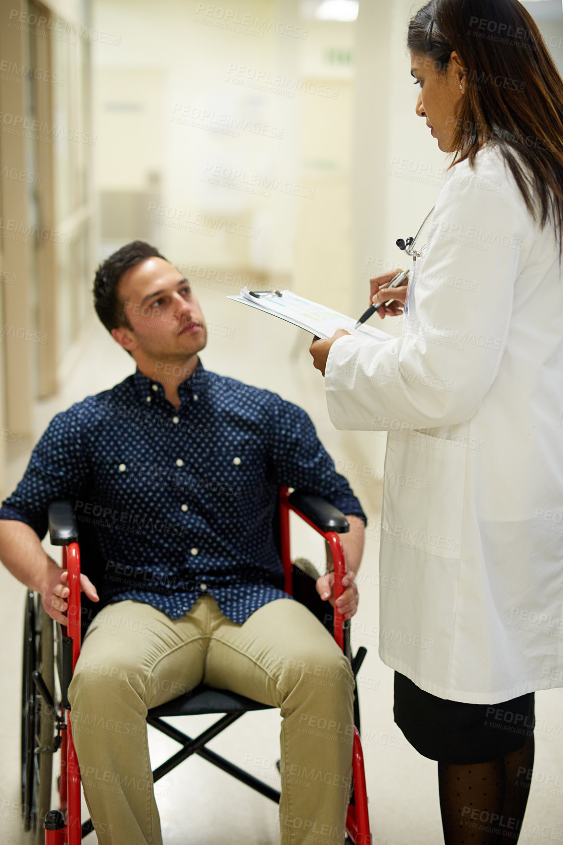 Buy stock photo Shot of a doctor attending to a patient sitting in a wheelchair in a hospital