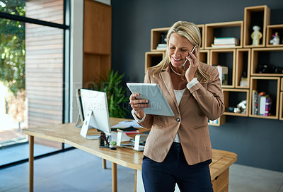 Buy stock photo Shot of a mature businesswoman using a digital tablet while talking on a cellphone in an office
