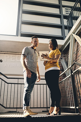 Buy stock photo Low angle shot of two young designers looking at a digital tablet while walking down a flight of stairs
