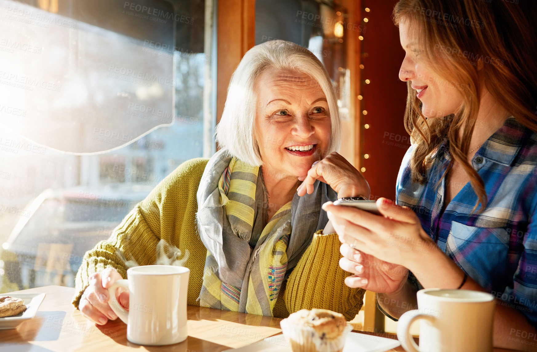 Buy stock photo Smile, senior woman and daughter with smartphone in cafe with social media for memories with relax. Post, funny and tech savvy people in restaurant with coffee, muffin and sunshine in retirement.