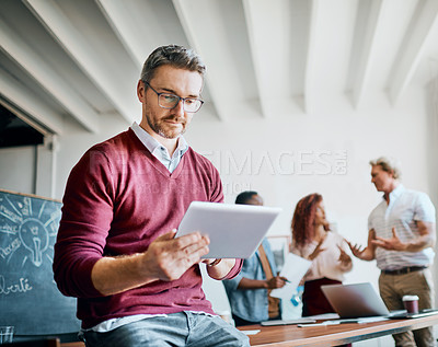 Buy stock photo Shot of a mature businessman working on his tablet while being seated in the office