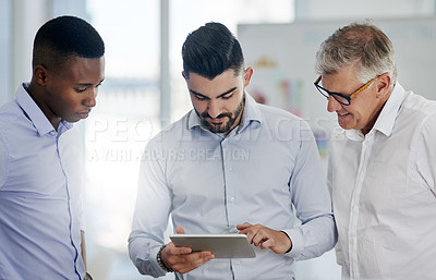 Buy stock photo Shot of a group of businessmen making use of a tablet while standing in the office at work