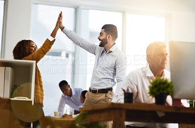 Buy stock photo Shot of two young work colleagues greeting each other with a high five while standing in the office
