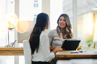 Buy stock photo Shot of two young businesswomen talking to each other while being seated in the office at work