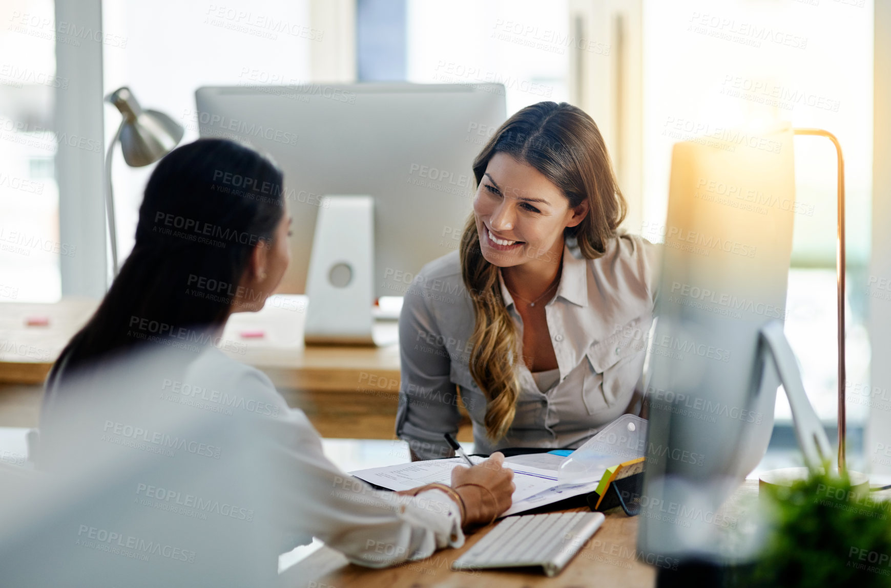 Buy stock photo Shot of two young businesswomen talking to each other while being seated in the office at work