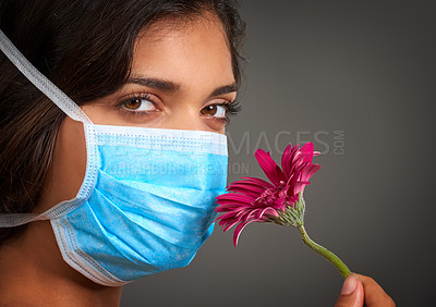 Buy stock photo Closeup of a young woman with a doctor's mask on looking at the camera and smelling a flower