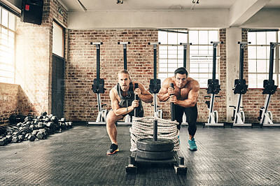 Buy stock photo Shot of two fit and determined young men making use of weights to workout in a gym together