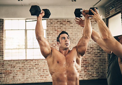 Buy stock photo Shot of two fit and determined young men helping each other out with weight exercises in a gym