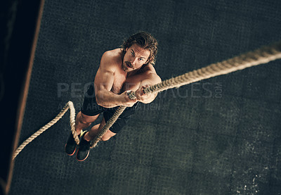 Buy stock photo High angle shot of a fit and determined young man climbing a rope for strength exercise in a gym