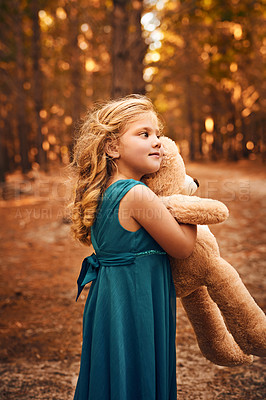 Buy stock photo Shot of a happy little girl holding her teddy bear and looking into the distance while standing outside in the woods