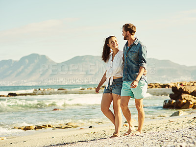 Buy stock photo Shot of a young married couple walking on the beach