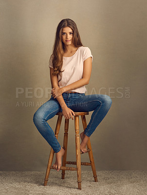 Buy stock photo Studio shot of a beautiful young woman sitting on a stool against a plain background