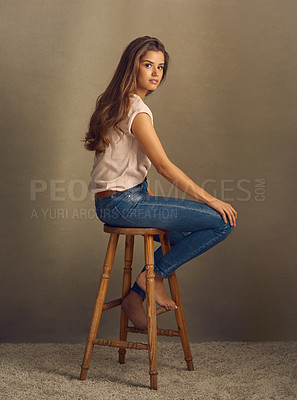 Buy stock photo Studio shot of a beautiful young woman sitting on a stool against a plain background