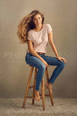 Buy stock photo Studio shot of a beautiful young woman sitting on a stool against a plain background