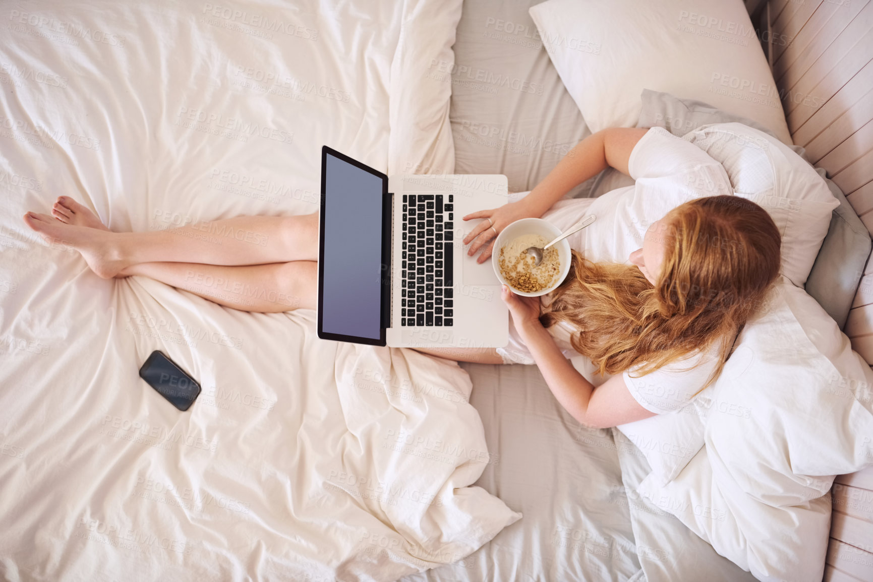 Buy stock photo Shot of a young woman eating breakfast and using a laptop at home