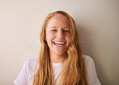 Buy stock photo Shot of a young woman smiling and standing against a wall at home