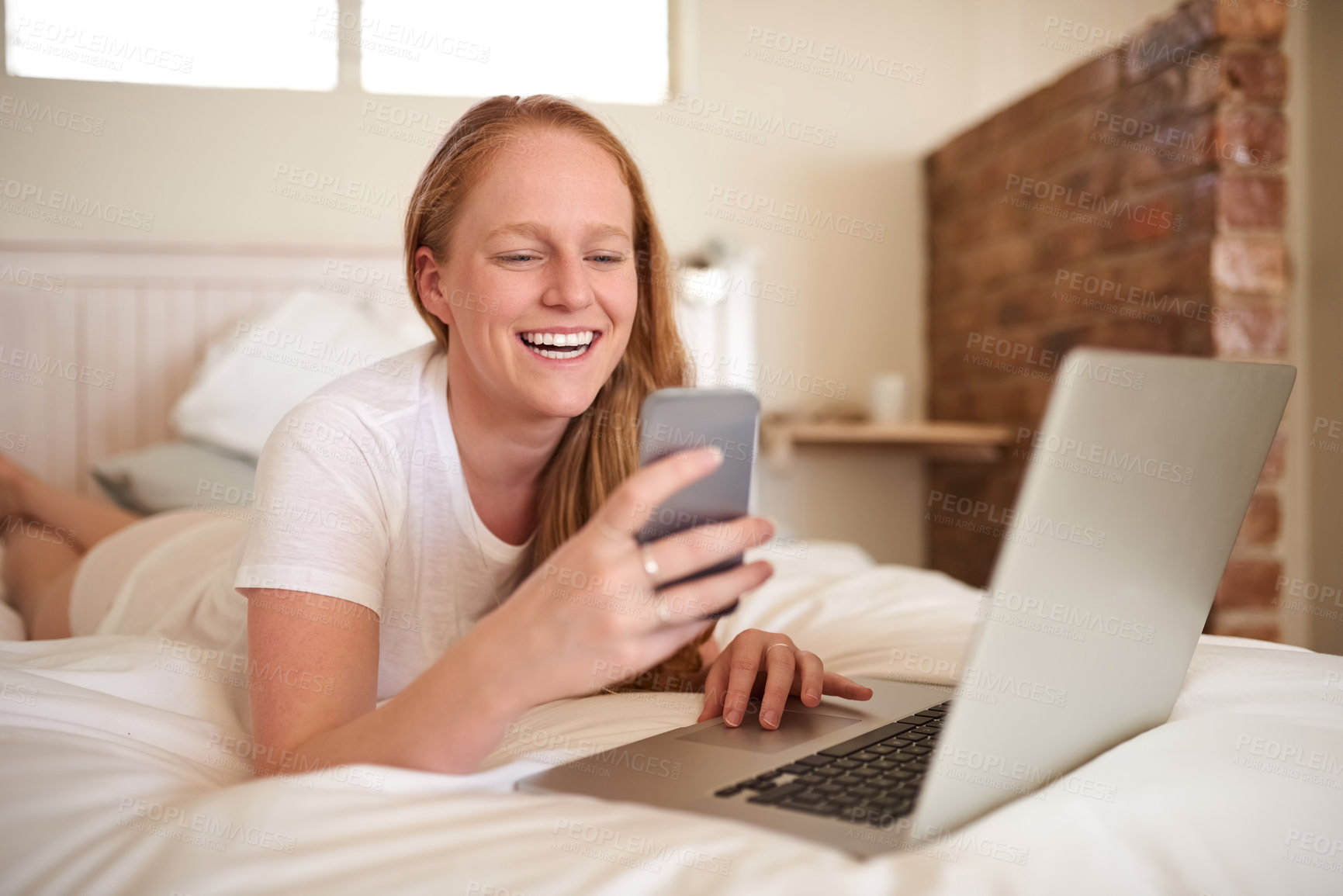 Buy stock photo Girl, laptop and phone for networking while on bed, searching and happy for browsing on social media. Laugh and smile at streaming site for entertainment, online in bedroom and post blog on website