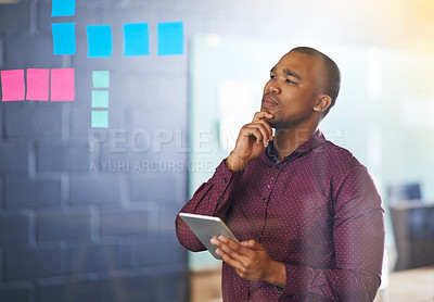 Buy stock photo Shot of a male designer holding a tablet looking at sticky notes on a glass wall