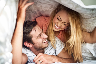 Buy stock photo Shot of a happy young couple having fun under a duvet in bed
